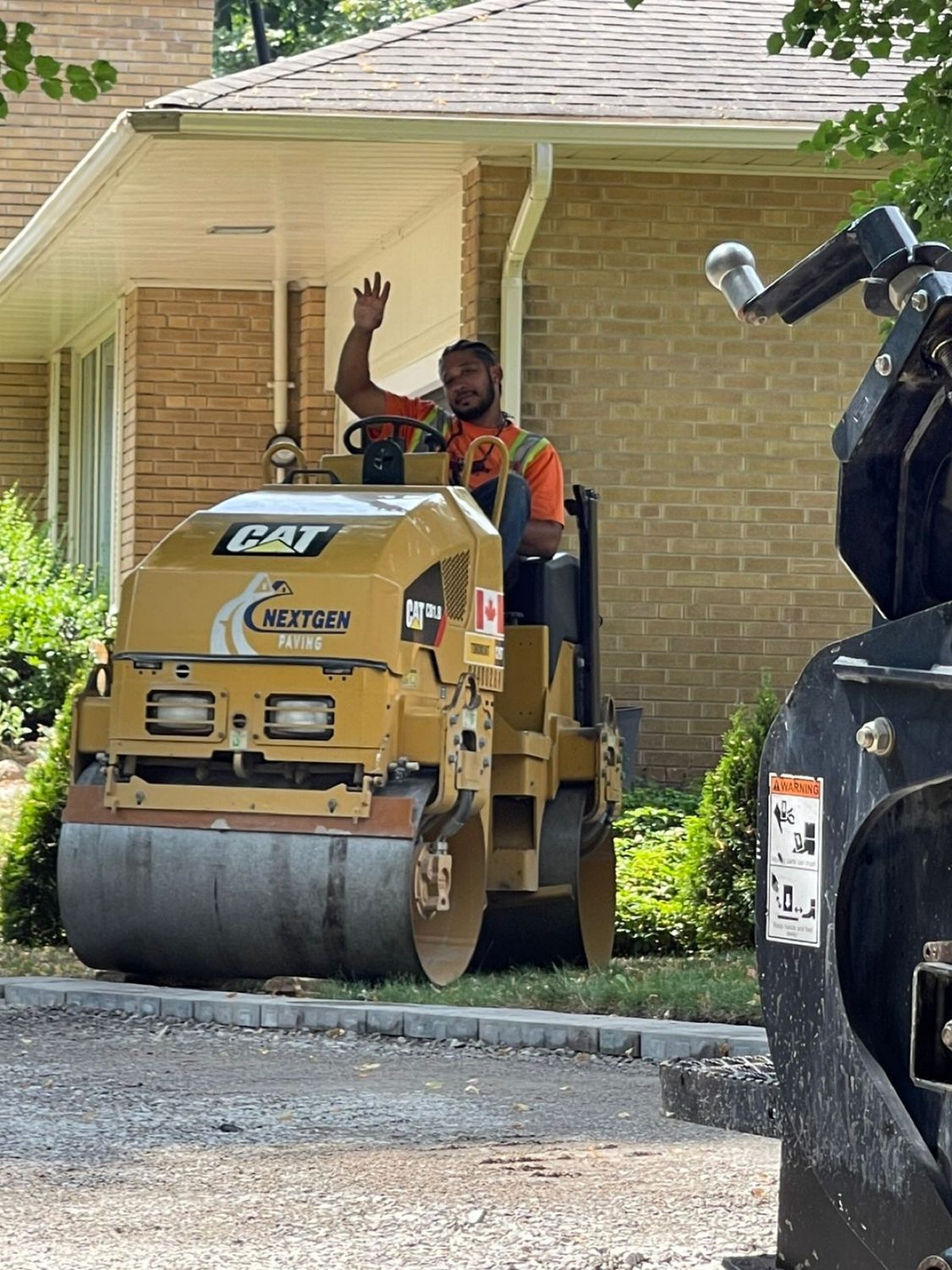 Next Gen Paving branded CAT roller at a residential job, operator waving